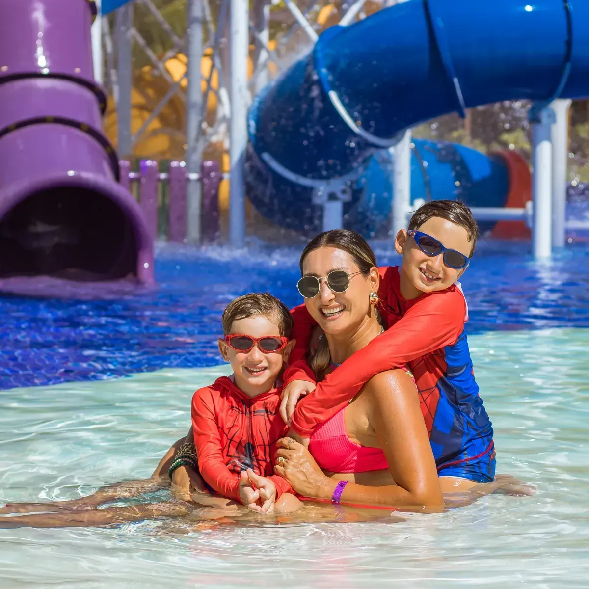 Mãe e dois filhos sorridentes se abraçando na piscina do parque aquático infantil do resort de praia Enotel Porto de Galinhas