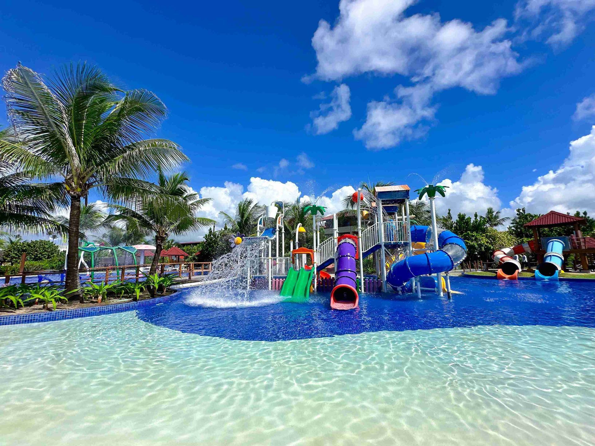 Parque aquático infantil com toboáguas coloridos, jatos d'água e piscina rasa cercada por coqueiros no resort all inclusive Enotel Porto de Galinhas.