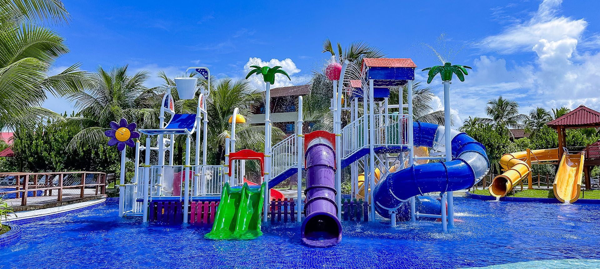 Estrutura completa do parque aquático infantil com toboáguas coloridos, escorregadores e balde interativo na piscina rasa do resort Enotel Porto de Galinhas.