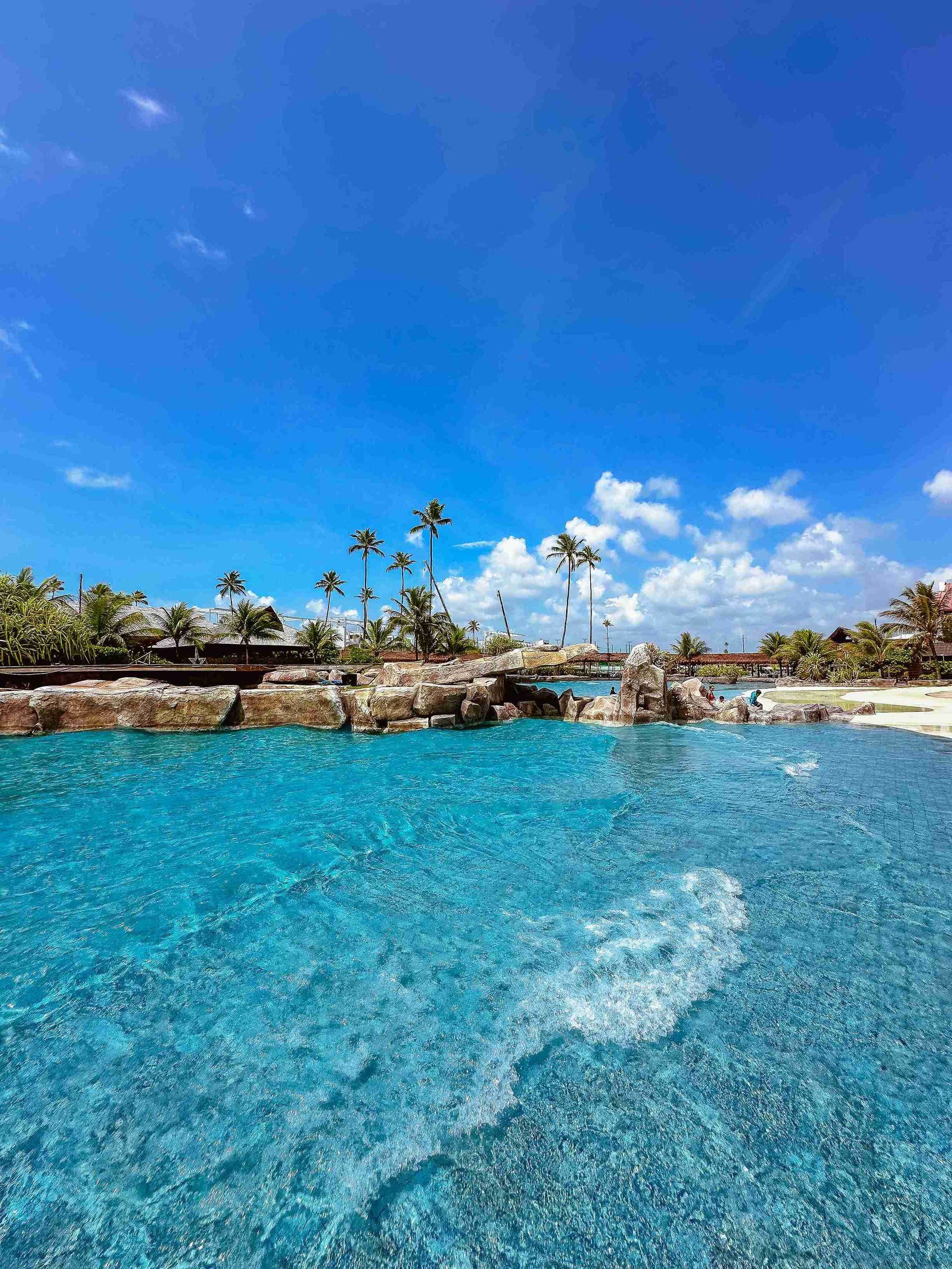 Piscina de ondas com águas cristalinas cercada por pedras artificiais e coqueiros em dia ensolarado no Enotel Porto de Galinhas