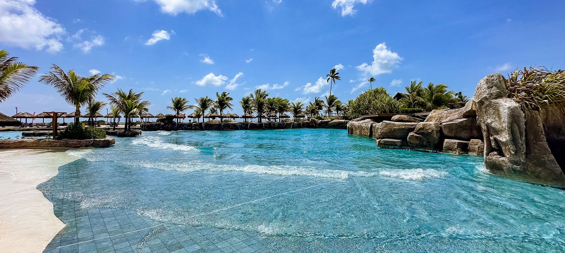 Vista da imensa piscina de ondas artificiais cercada por pedras artificiais e coqueiros no resort Enotel Porto de Galinhas