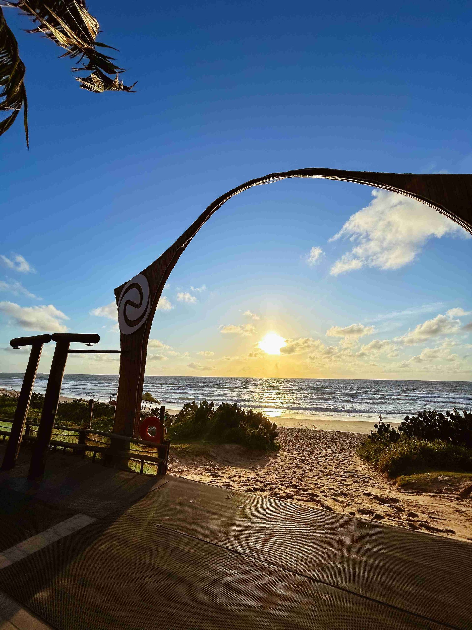 Portal de acesso exclusivo à praia de Porto de Galinhas durante o amanhecer com o sol refletindo no mar, no resort Enotel