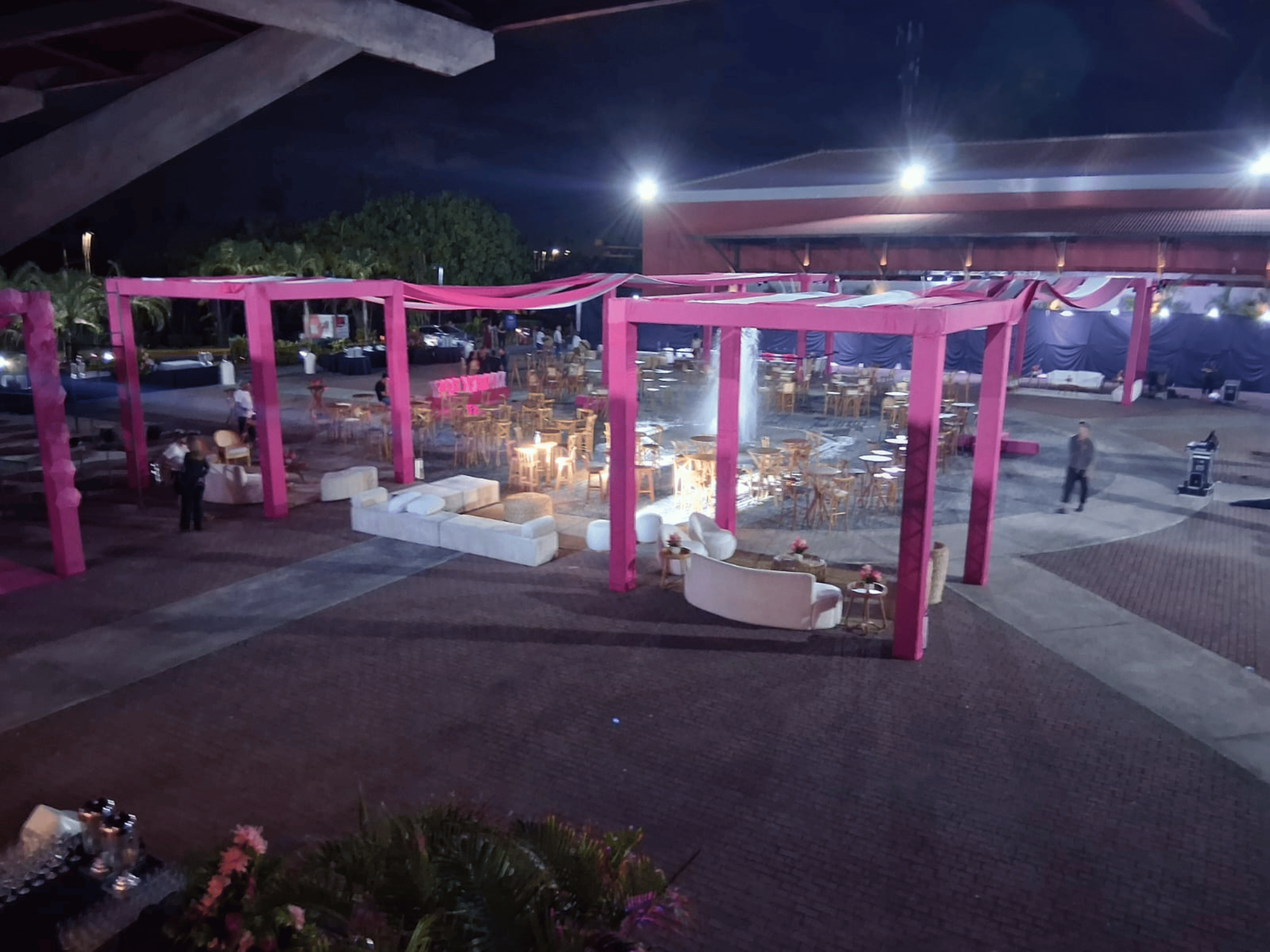 Espaço de eventos ao ar livre na Praça Dom Pedro com lounges cobertos por tecidos rosa, sofás brancos e mesas bistrô ao redor da fonte iluminada