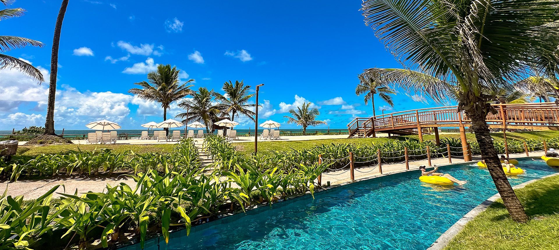 Hóspedes em boias amarelas descendo o circuito de rio lento cercado de jardins no resort all inclusive Enotel Porto de Galinhas