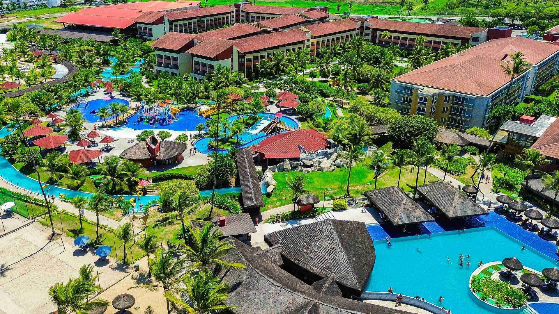 Vista aérea ampla de drone mostrando a megaestrutura dos blocos de apartamentos e todo o complexo aquático com piscinas e parque infantil do Enotel Porto de Galinhas