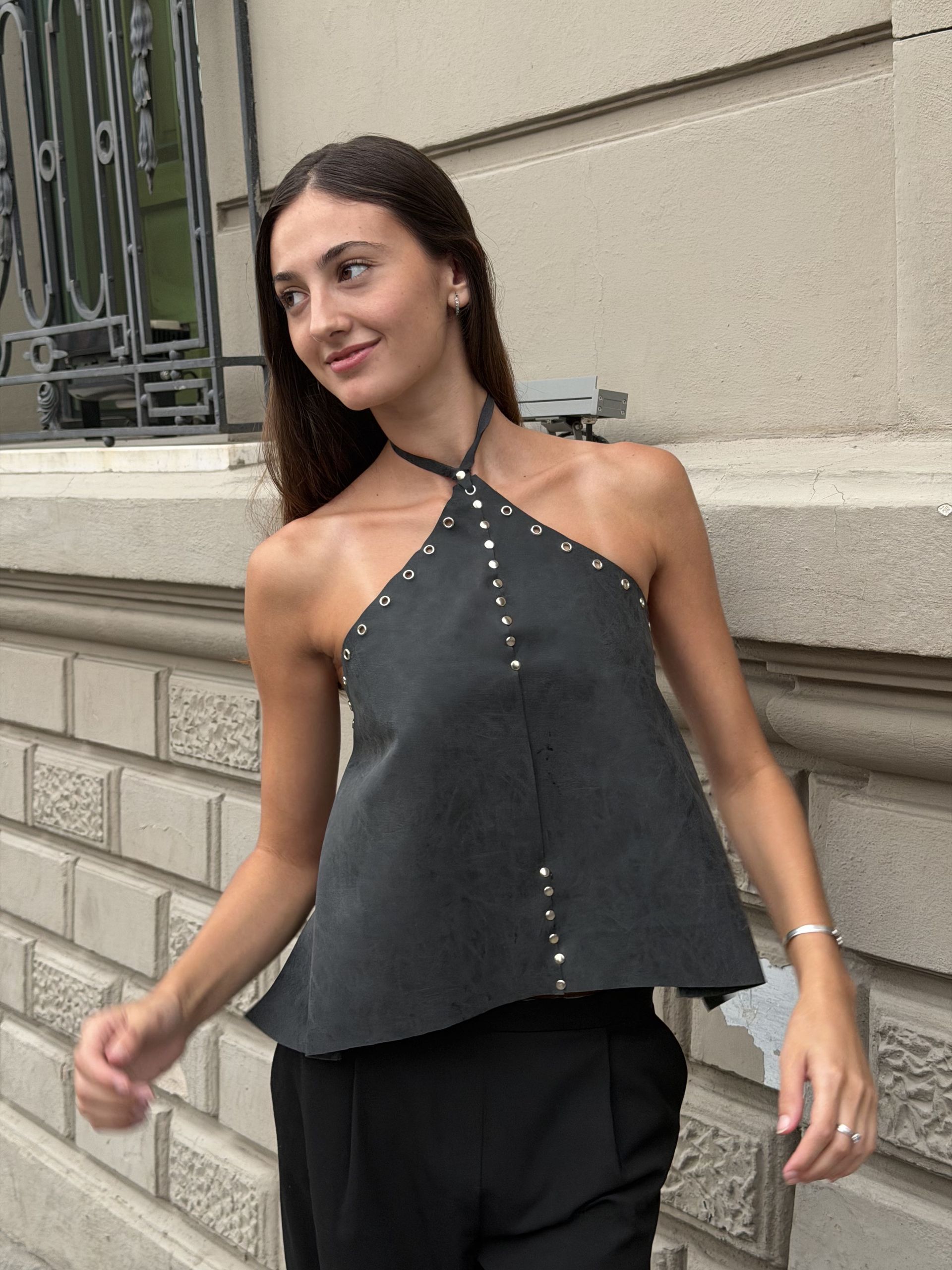 Mujer con un top gris con tachuelas plateadas y pantalones negros, de pie afuera.