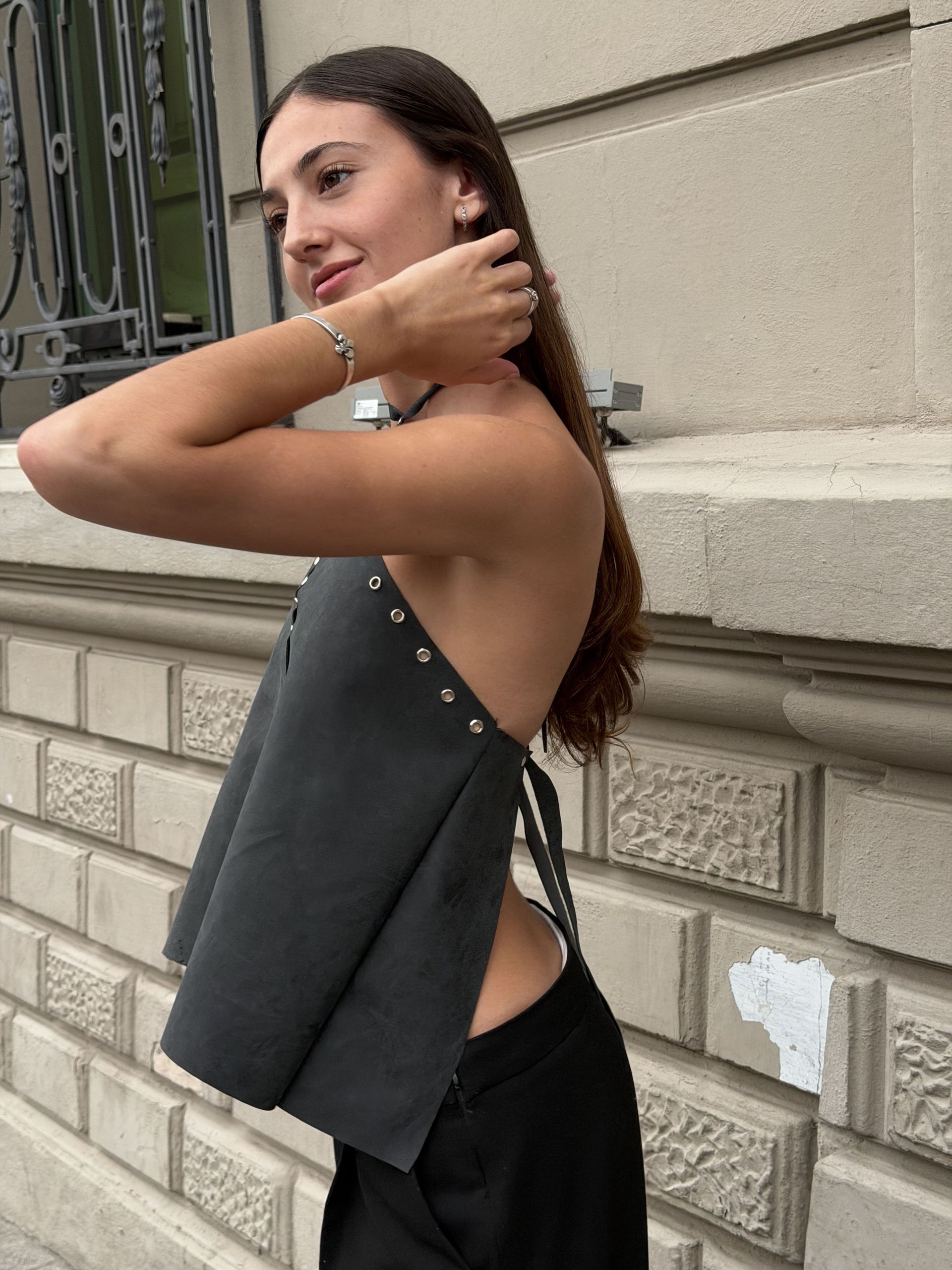 Mujer con un top gris con tachuelas plateadas y pantalones negros, de pie afuera.