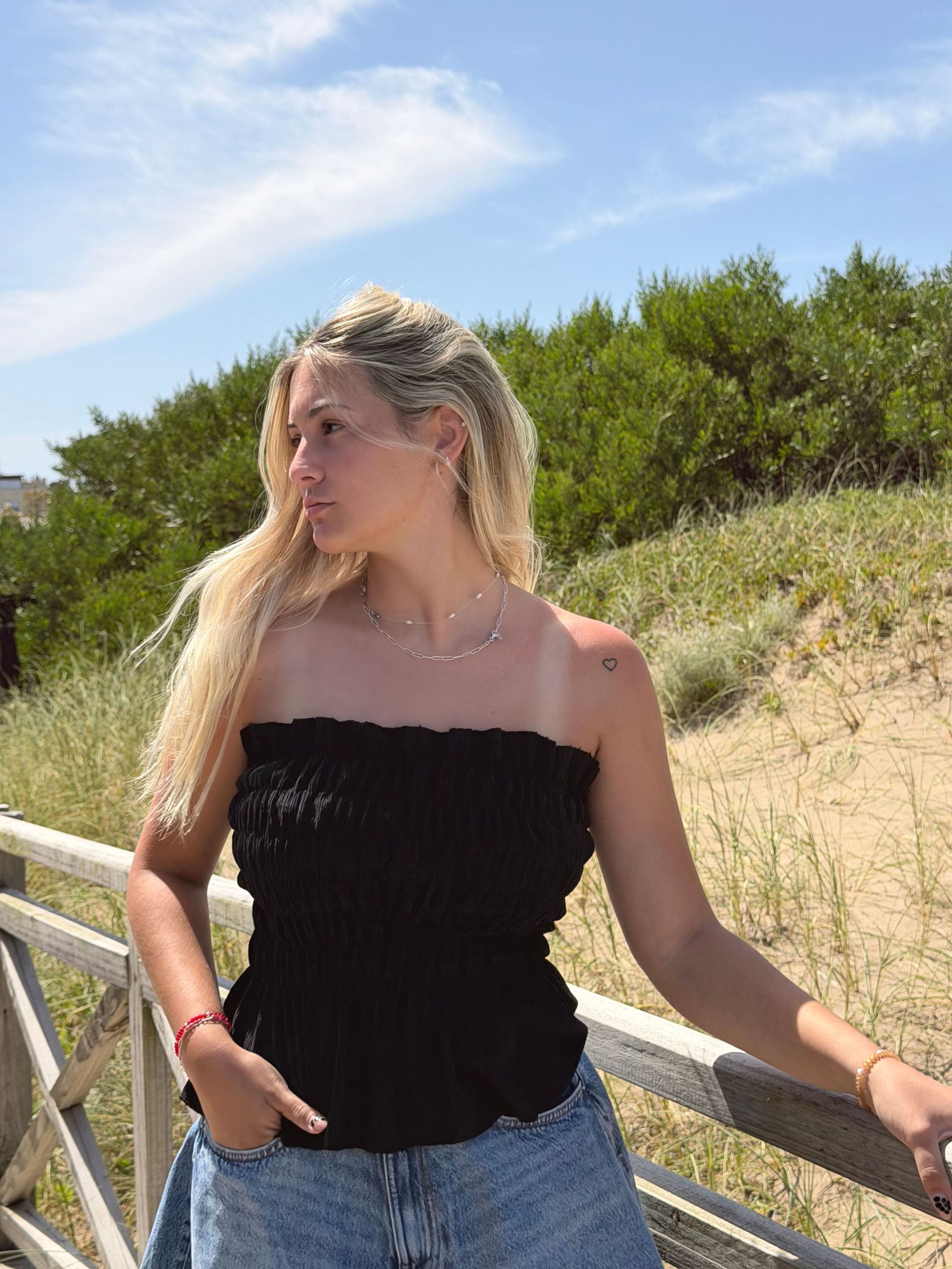 Persona rubia con top negro y shorts vaqueros, de pie sobre una pasarela de madera