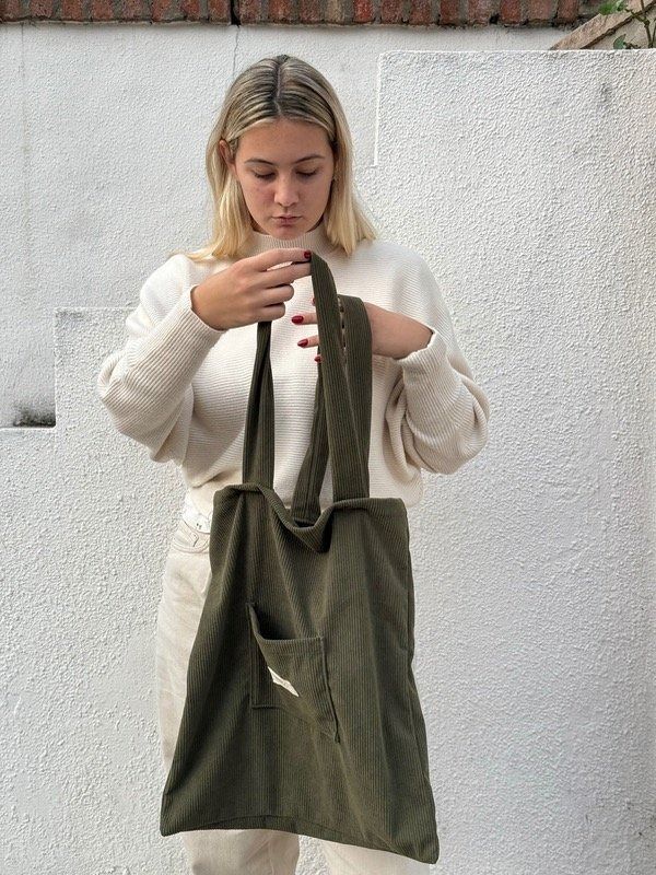 Mujer sosteniendo un bolso tote grande de color verde oliva frente a una pared blanca texturizada.