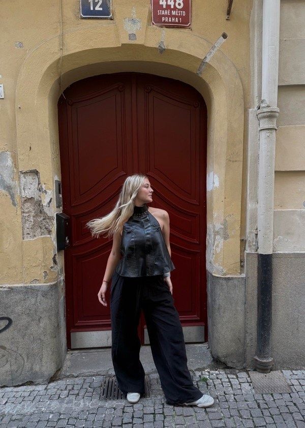 Una mujer con blusa y pantalones oscuros da vueltas frente a una puerta roja.