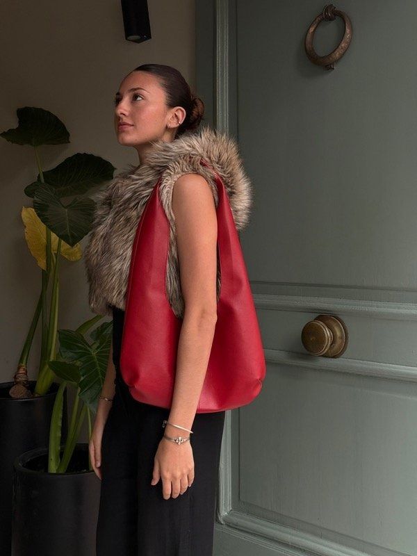 Mujer con chaleco de piel y bolso rojo, de pie junto a una puerta verde.