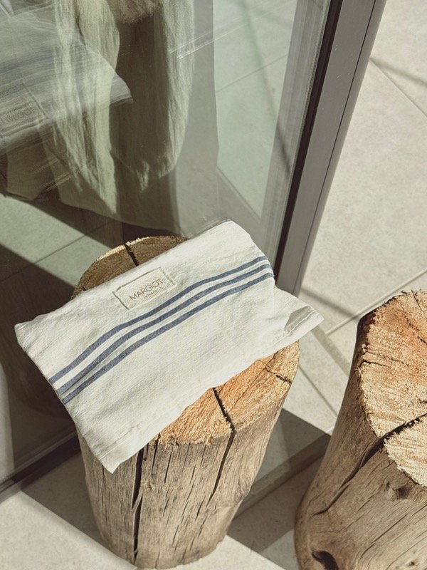 Toalla blanca con rayas azules sobre un tocón de madera cerca de una ventana.