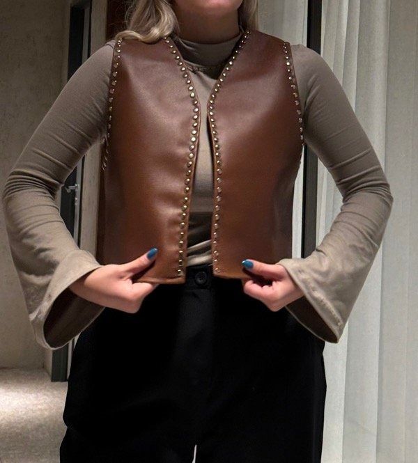 Mujer mirando su reloj en un pasillo, vestida con un chaleco marrón