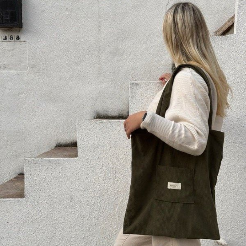 Mujer que sostiene un bolso tote de pana verde oscuro, de pie sobre unos escalones blancos.