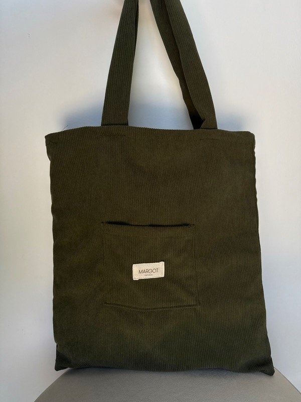 Mujer sosteniendo un bolso tote grande de color verde oliva frente a una pared blanca texturizada.