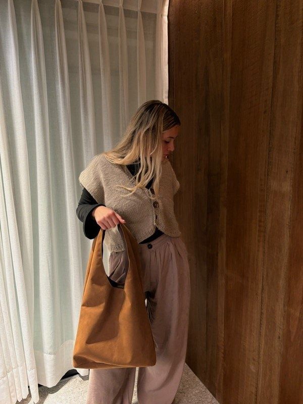 Persona que lleva una bolsa de tela marrón, viste un chaleco de punto y pantalones marrones.