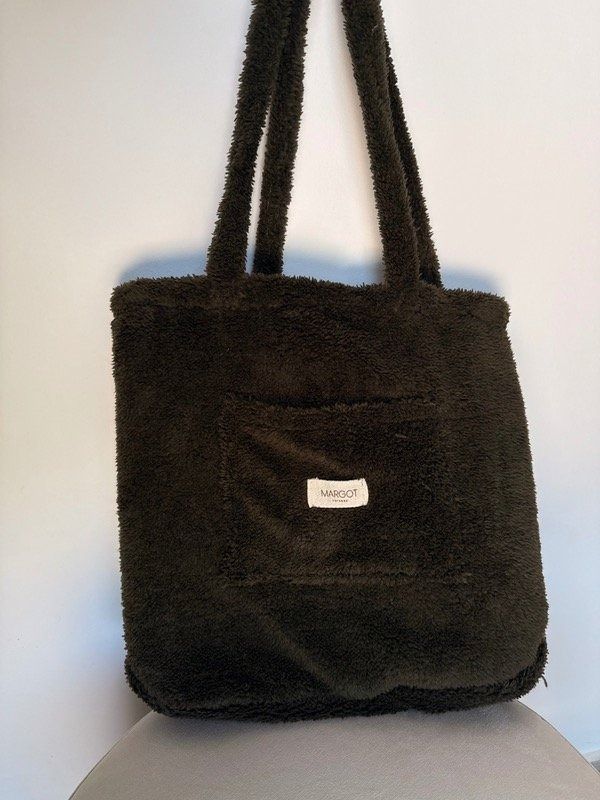 Mujer vestida con suéter y pantalones blancos, sosteniendo un bolso tote