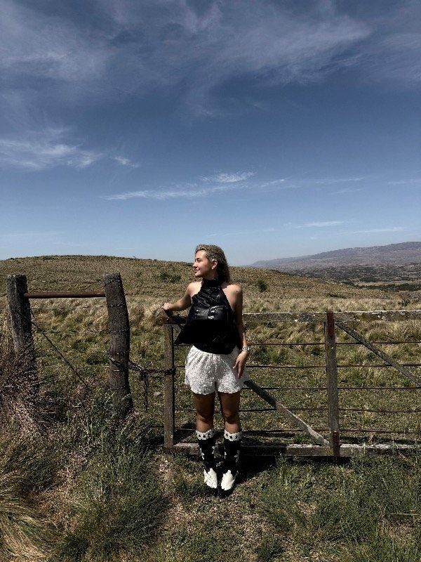 Una mujer con blusa y pantalones oscuros da vueltas frente a una puerta roja.