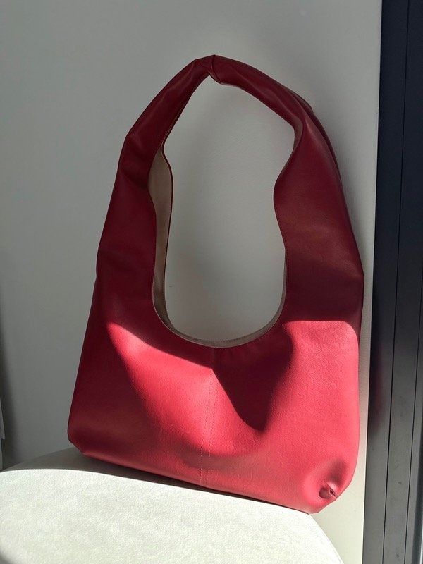 Mujer con chaleco de piel y bolso rojo, de pie junto a una puerta verde.