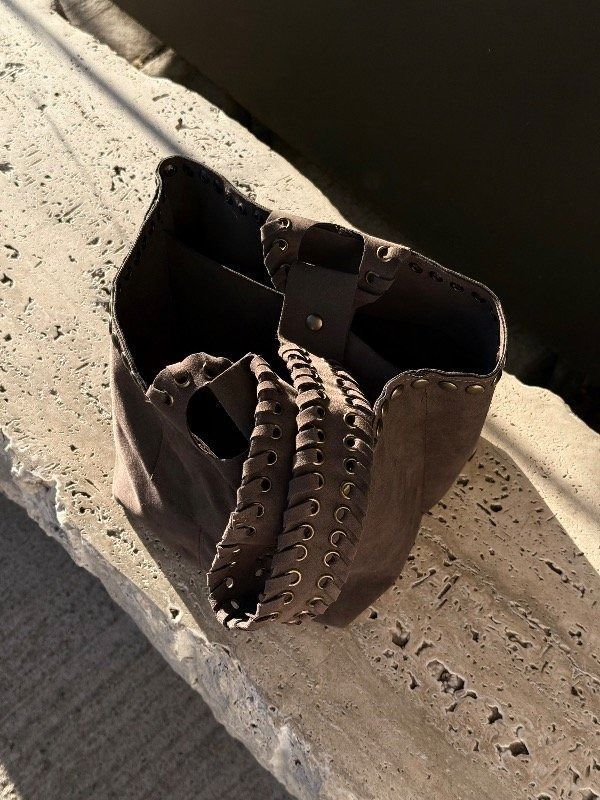 Bolso de cuero marrón sobre un bloque de piedra tosca, contra una pared de madera negra.