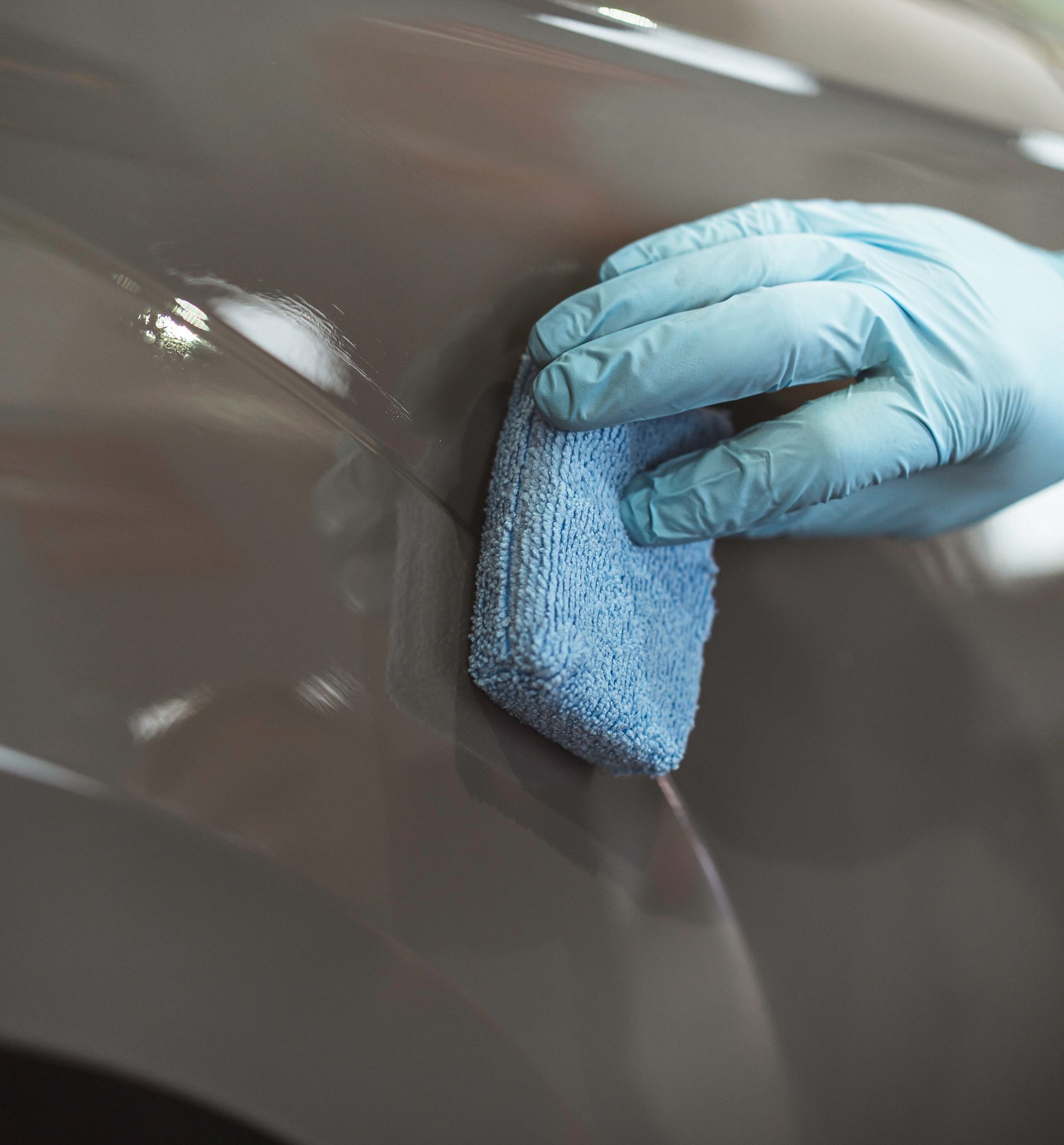 A person wearing blue gloves is wiping ceramic coating on a car with a blue sponge.