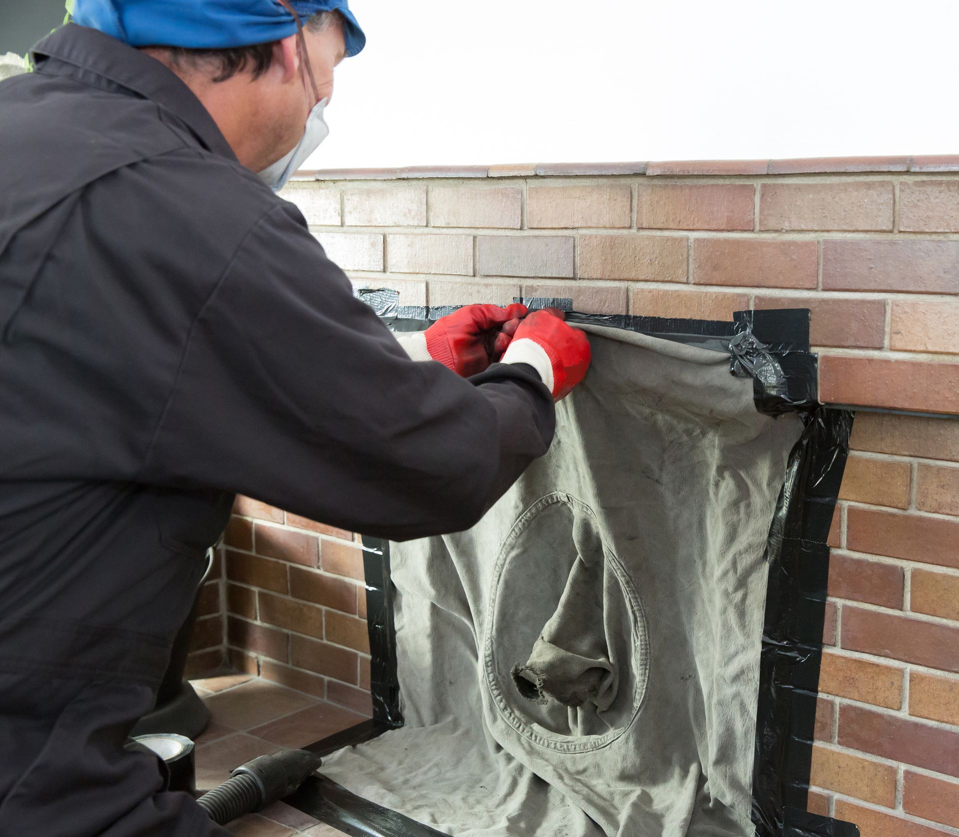 Technician sealing fireplace with protective cover during chimney cleaning preparation work.