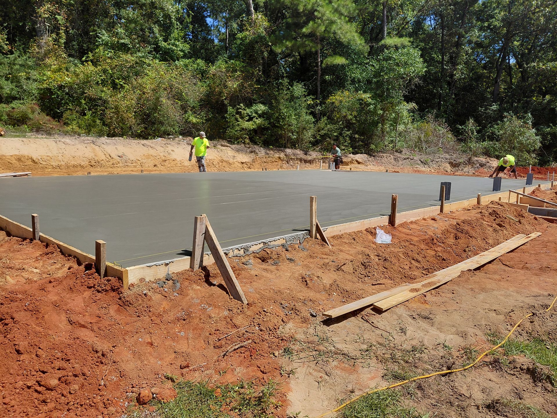 Workers smoothing wet concrete for a foundation, surrounded by dirt and wooden forms.