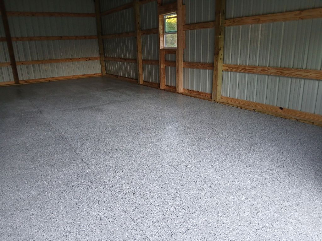 Interior of a building with a gray speckled concrete floor and corrugated metal walls. Wooden beams frame the structure.