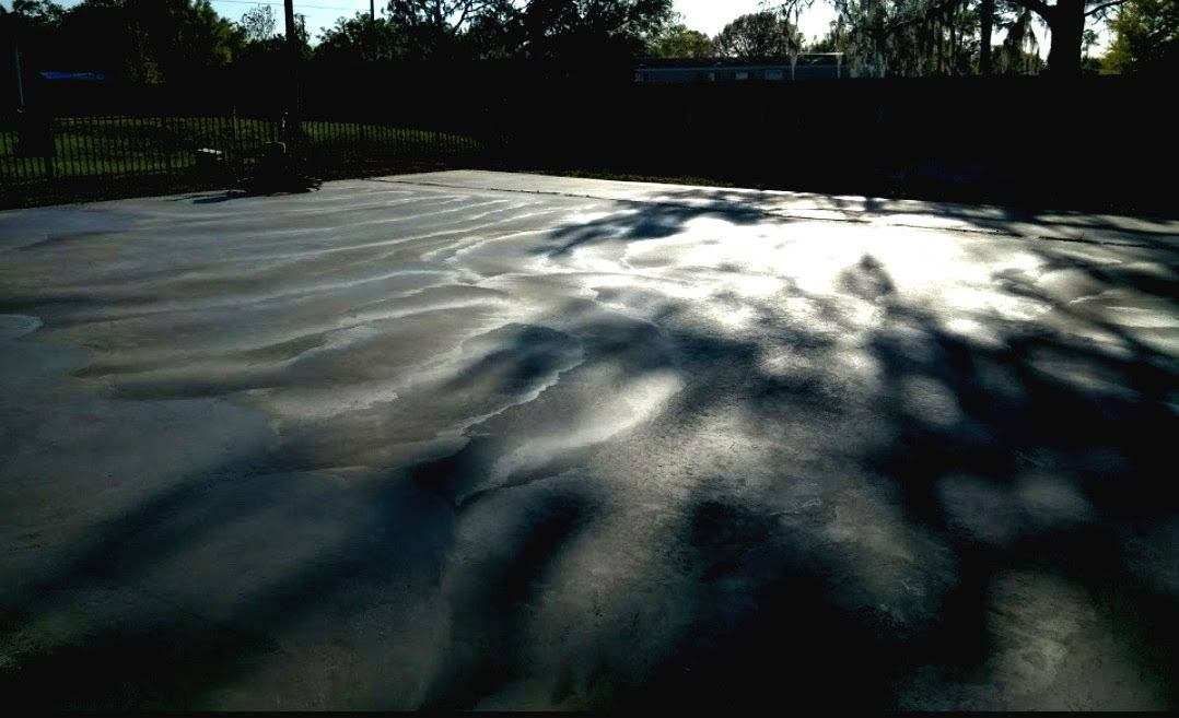 Dark asphalt with textured surface, dappled sunlight and shadows from trees.