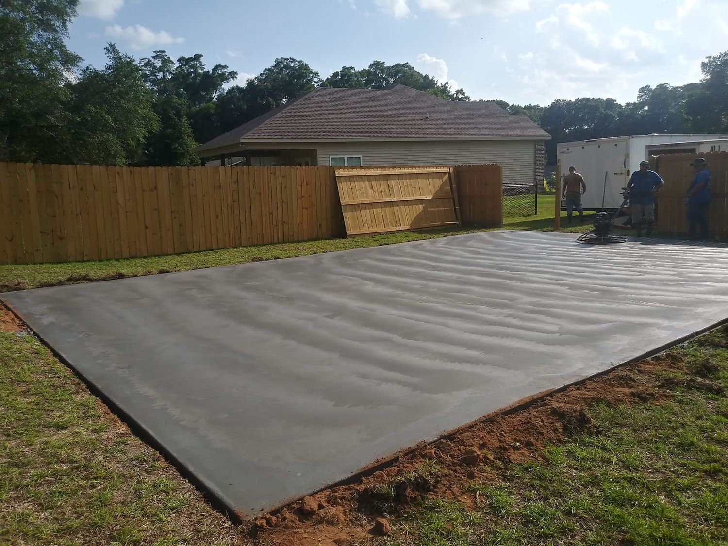 Black tarp laid on the ground in a backyard. Two people stand near a small shed.