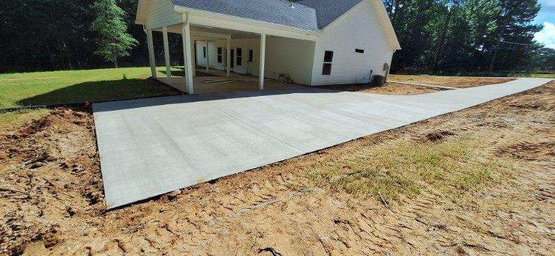 A newly poured concrete driveway leads to a white house with a covered porch.