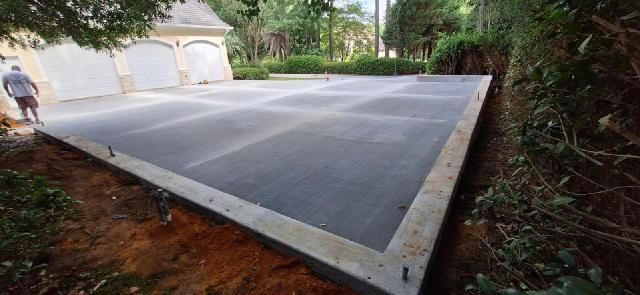 A recently poured concrete pad next to a building with garage doors. A person stands on the edge.