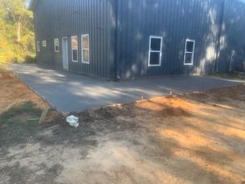 New concrete patio next to a dark blue metal building on a dirt lot.