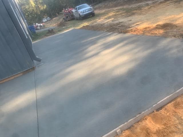 Newly poured concrete slab next to a building, a vehicle is in the background.