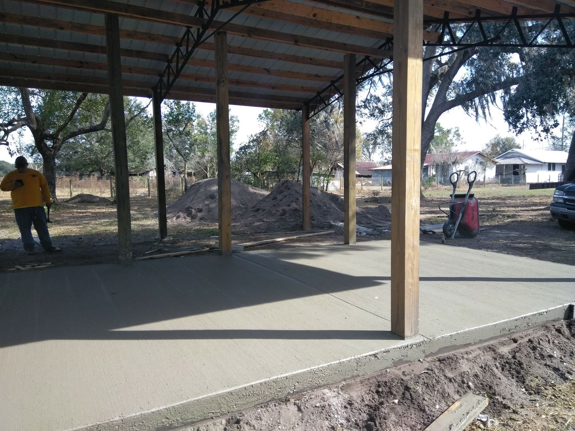 New concrete slab under a wooden structure with posts. A person is visible in the distance.