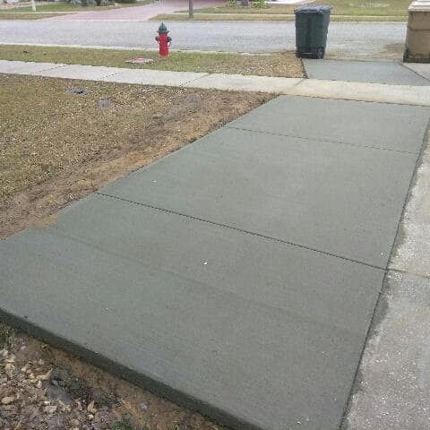 Newly poured concrete sidewalk with cut lines; dry grass and street in background.