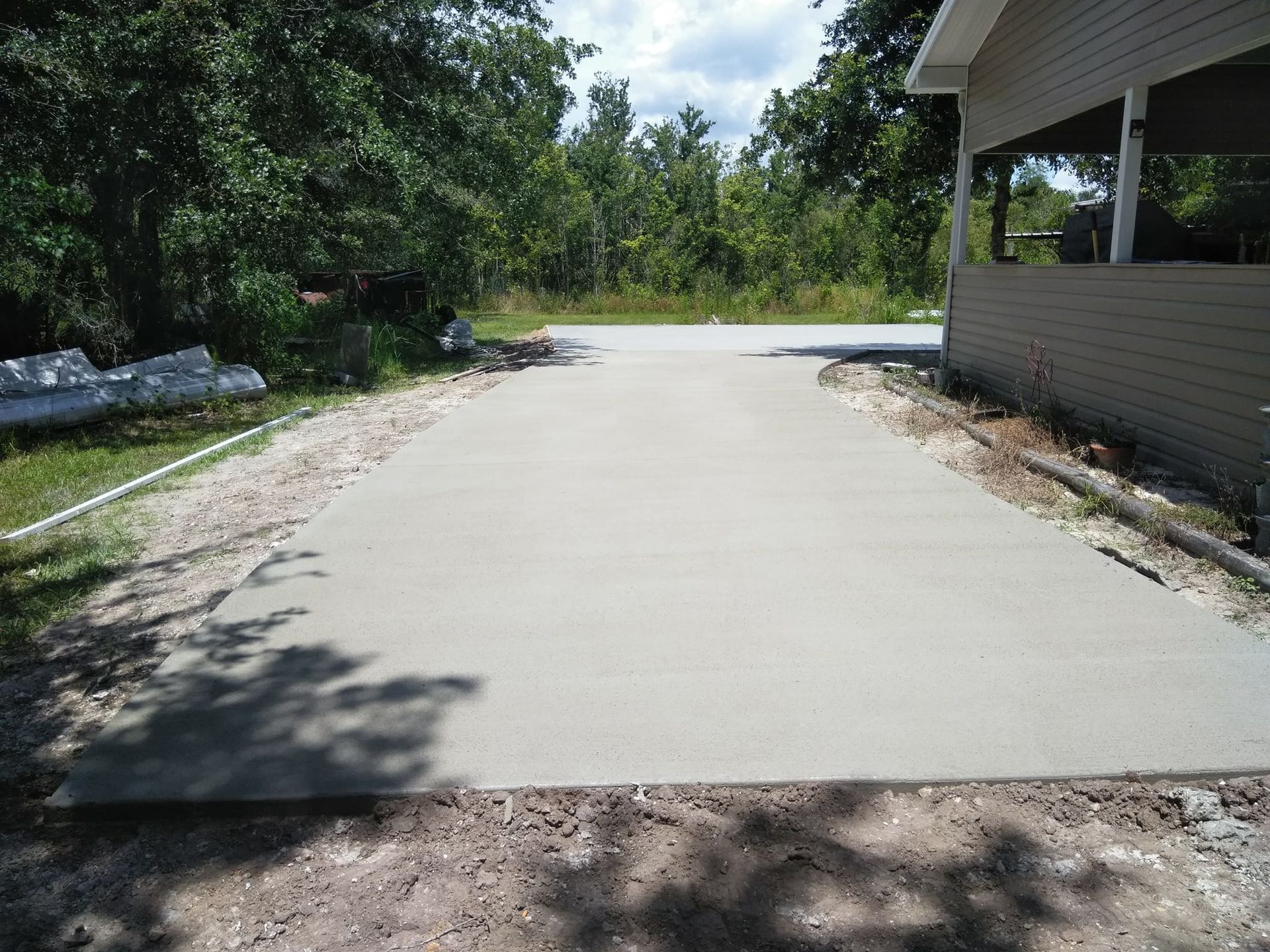 Newly poured concrete driveway next to a building, surrounded by dirt and trees.