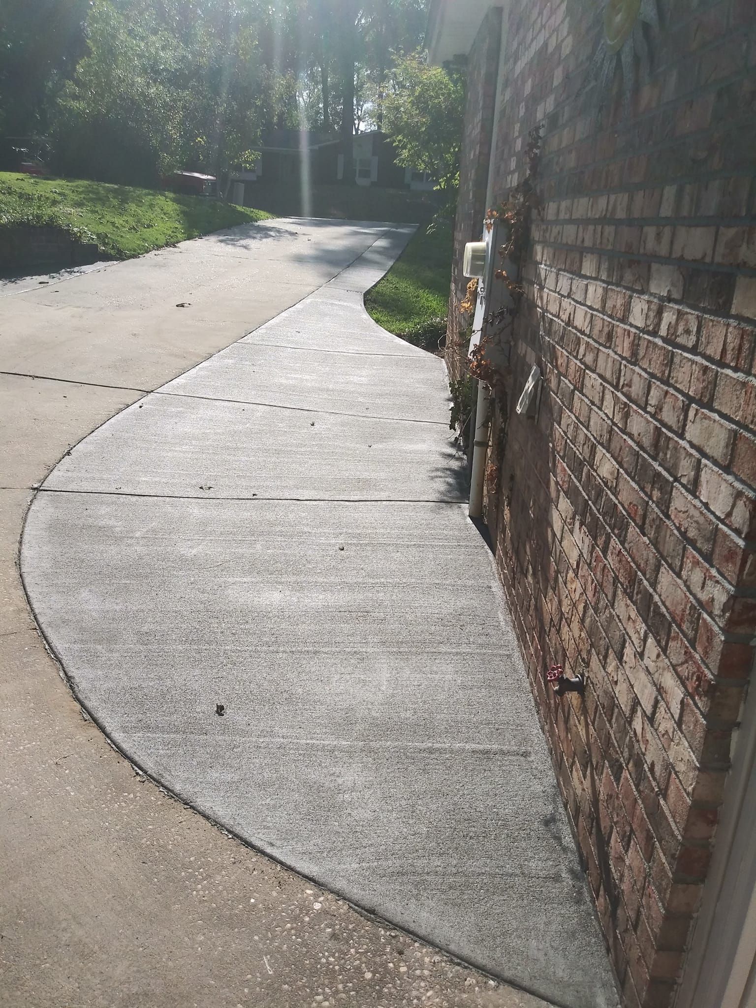 Dark gray concrete walkway next to a red brick building, curving to meet a driveway.