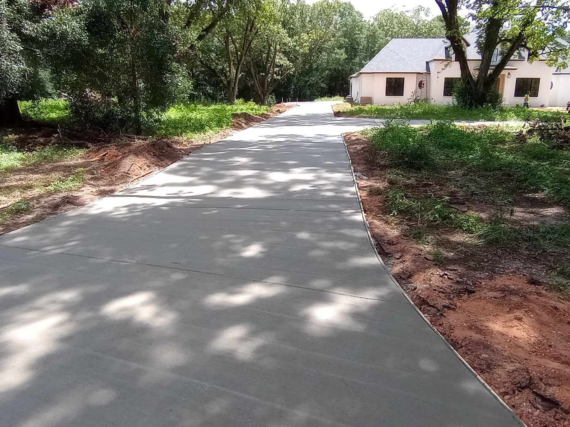 Newly poured concrete driveway leading to a light-colored house with a grassy yard and trees.