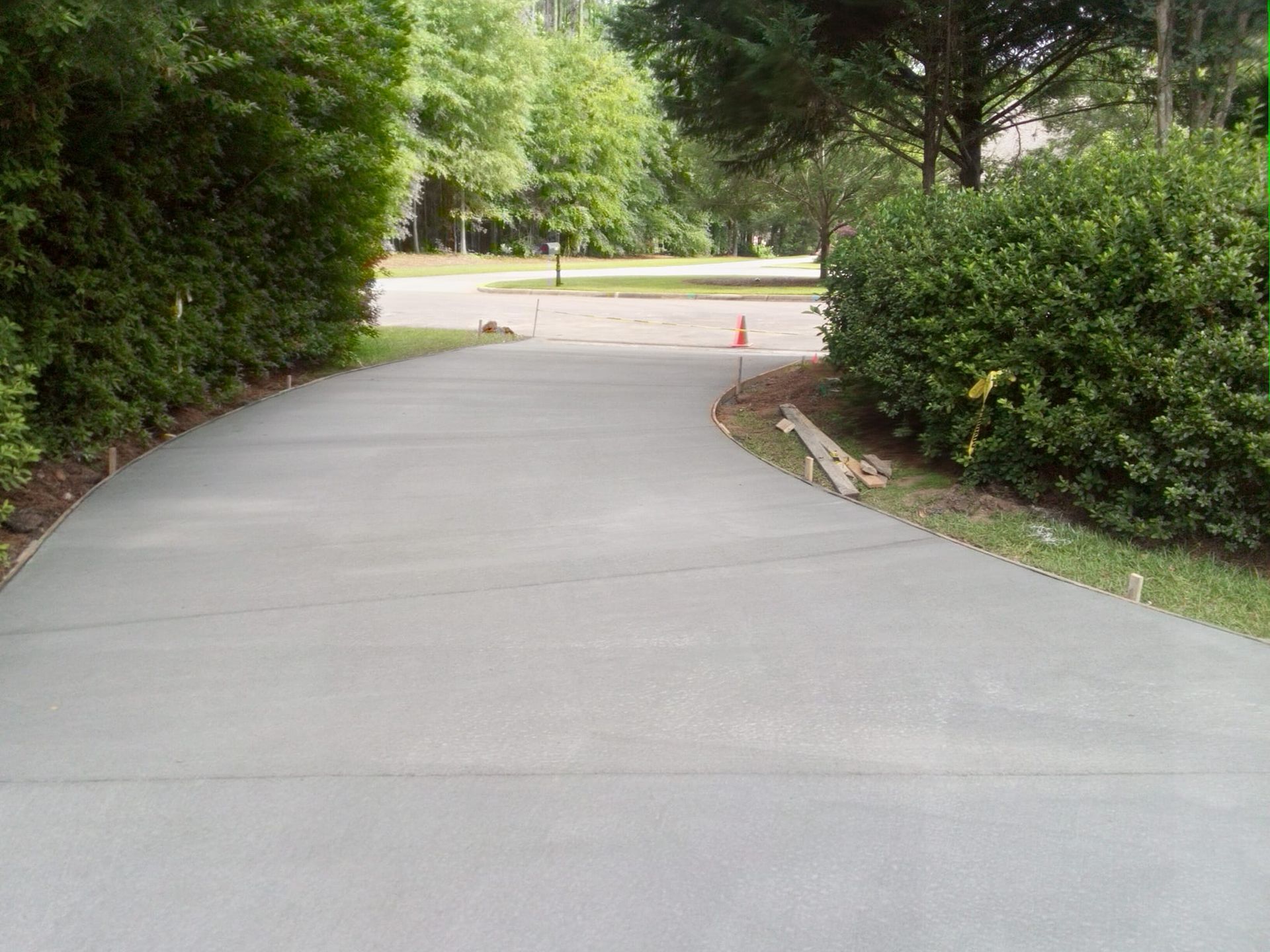 Newly poured concrete driveway curves toward trees and a street.