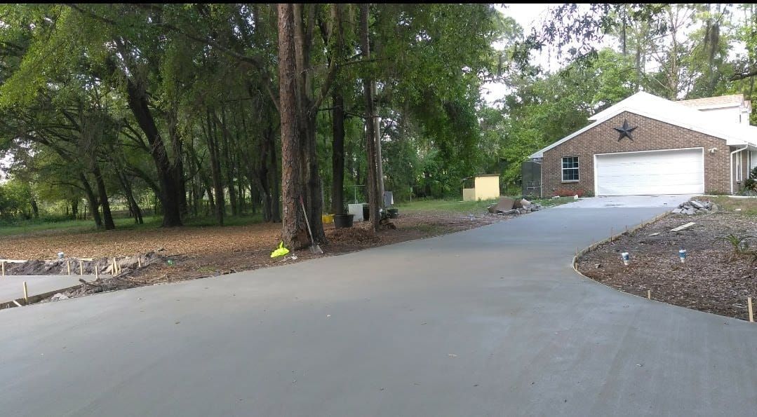 New concrete driveway leading to a brick garage, with trees and a grassy yard visible.
