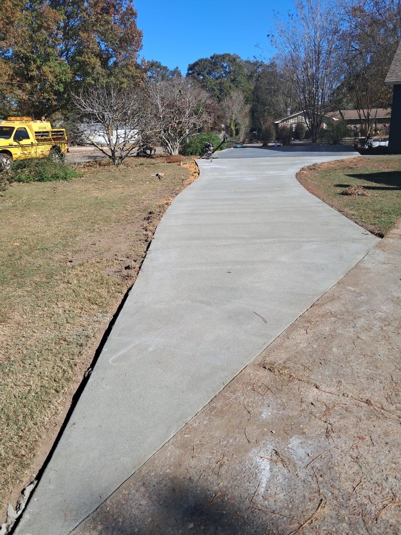 Concrete driveway curving through a grassy yard, with a yellow vehicle in the background.