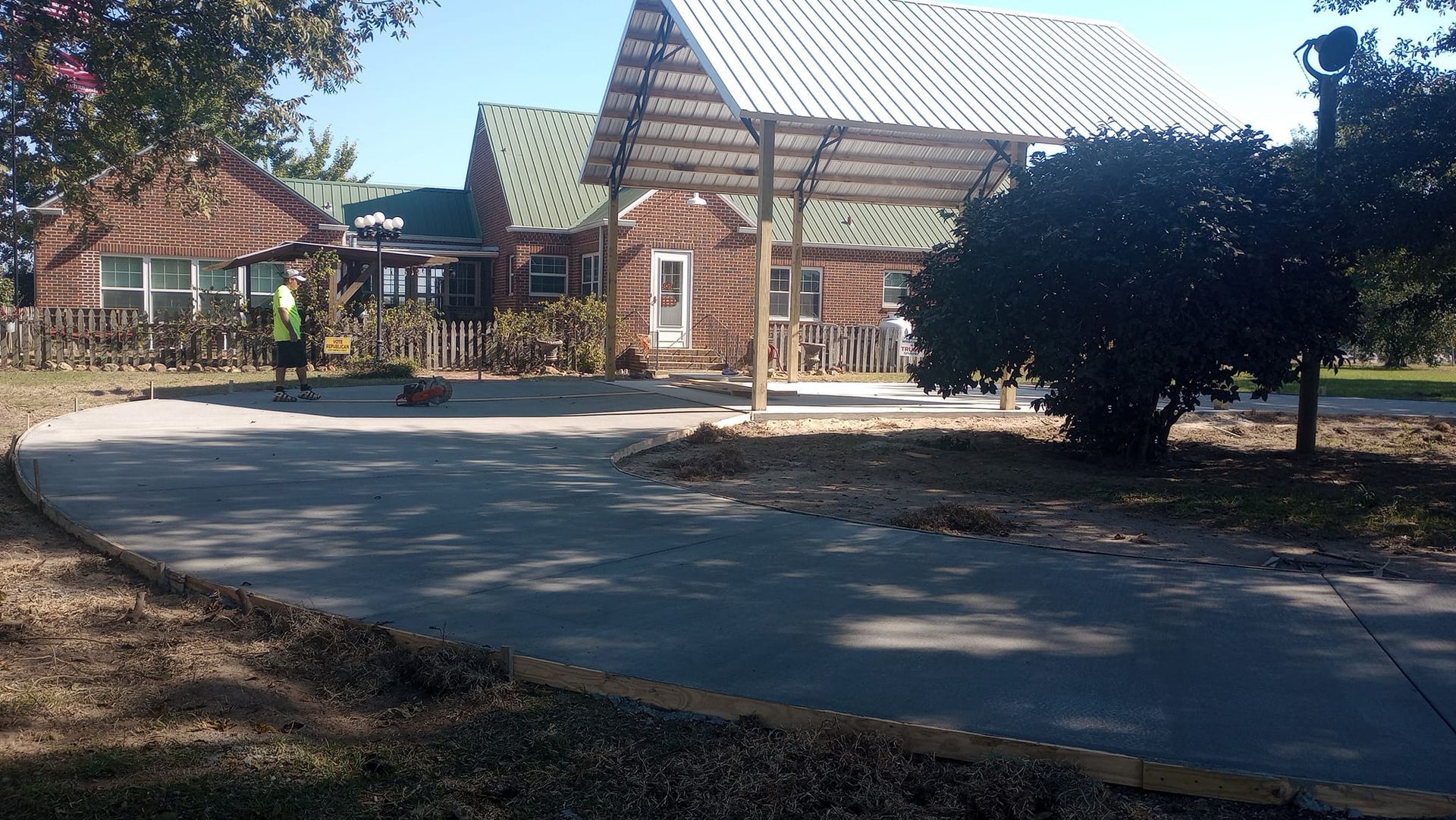 A house with a driveway. A person wearing a vest stands on the left. Sunny day.