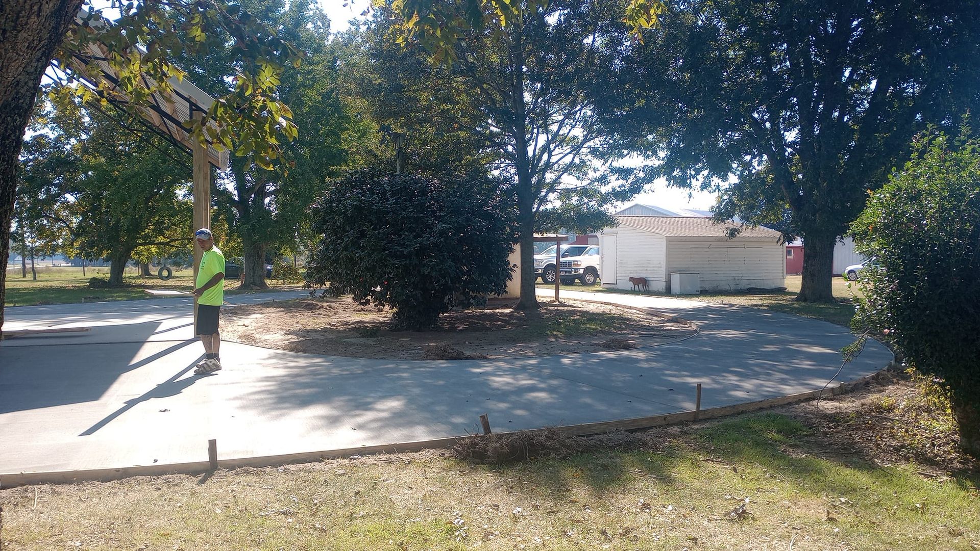 Person standing on a curved concrete path near a basketball hoop and a small building with trees.