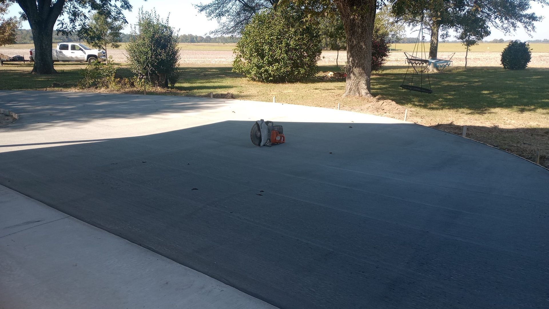 A stack of orange bricks on a gray concrete slab, trees and field in the background.