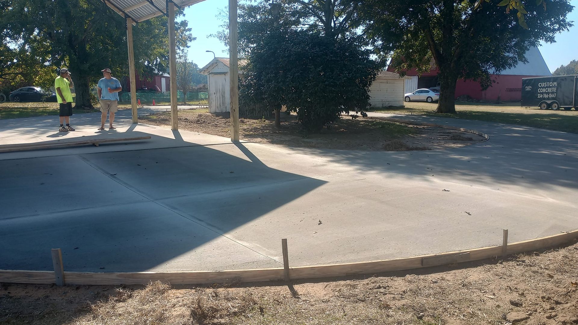 Concrete driveway being constructed; two people nearby, sunny day.