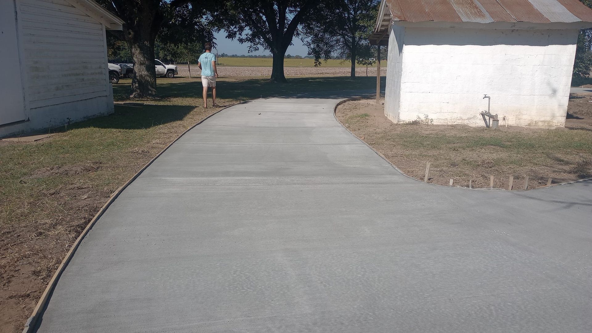 Concrete driveway curves toward distant tree; white buildings on either side.