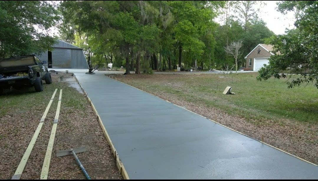Newly poured concrete driveway with wooden forms, leading to a house.