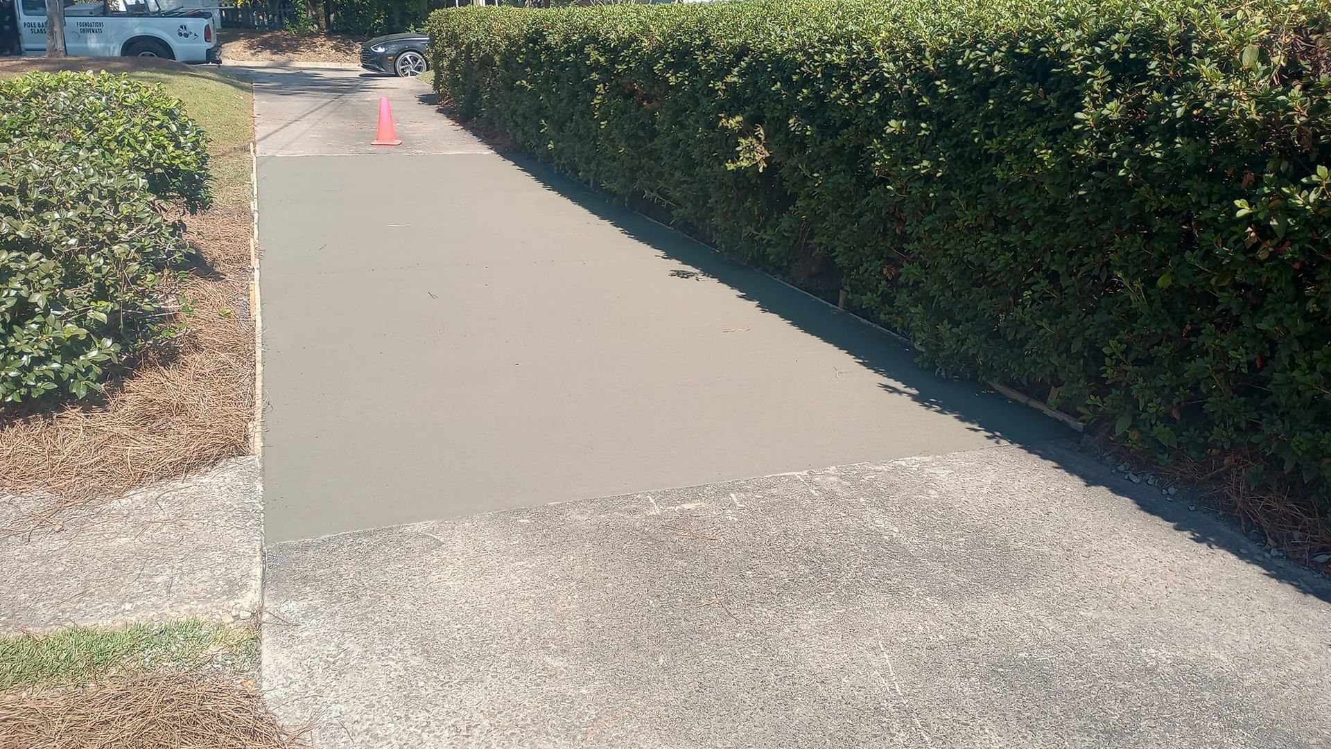 New concrete patch on a driveway bordered by a hedge and grass.