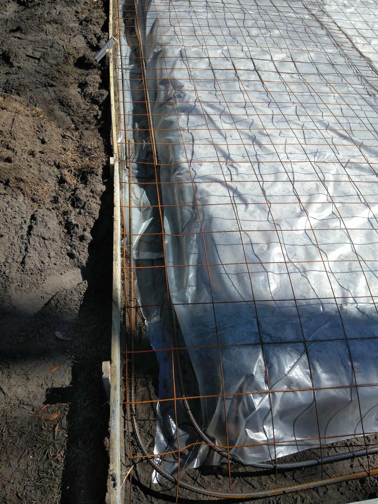 Construction site: Plastic sheeting over rebar grid within wooden frame, in dirt.